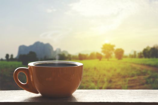 Hot Black hot coffee with smoke. Ceramic brown glass placed on an outdoor wood table. The background is a landscape of nature with mountains and farmland with vintage colors. Business ideas