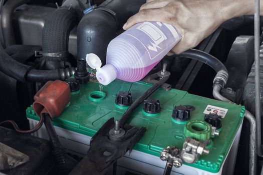 Hands of technician adding water to battery in a service center