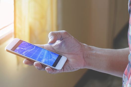 The businessman is holding a smartphone with touch screen to check the stock with a stylish white mobile phone in his house