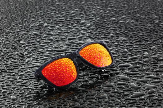 A pair of orange sunglasses with water droplets on wet surface