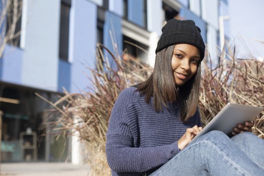 Portrait of African American young woman wearing a wool cap standing on the street while using a mobile phone