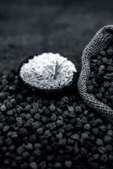 Close up of a jut bag full of chickpeas or grams in it and its floor or besan ka atta in a clay bowl on brown colored surface.