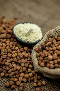 Close up of a jut bag full of chickpeas or grams in it and its floor or besan ka atta in a clay bowl on brown colored surface.