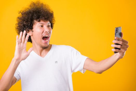 Portrait asian handsome man curly hair taking selfie with mobile phone isolated on yellow background