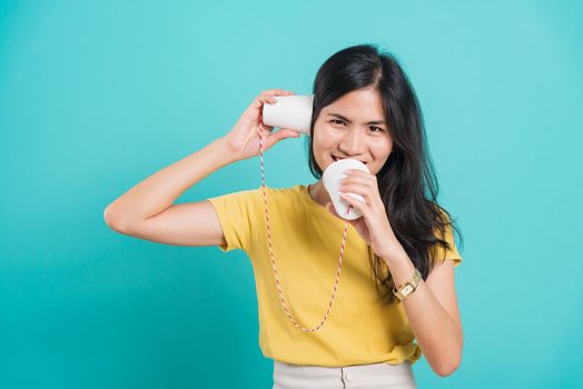 Portrait happy Asian beautiful young woman smile white teeth standing wear yellow t-shirt, She holding paper can telephone for talking, studio shot on blue background with copy space for text