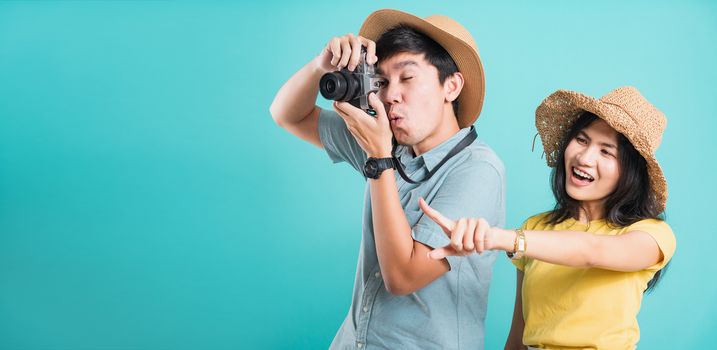 Happy Asian excited couple young beautiful woman point finger and handsome man holding camera shot photography in summer holiday travel tourists isolated on blue background with copy space for text