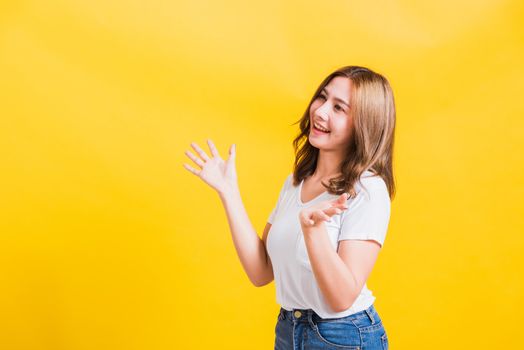 Asian Thai happy portrait beautiful cute young woman standing wear t-shirt her winning and surprised excited screaming open mouth showing hands, studio shot isolated yellow background with copy space