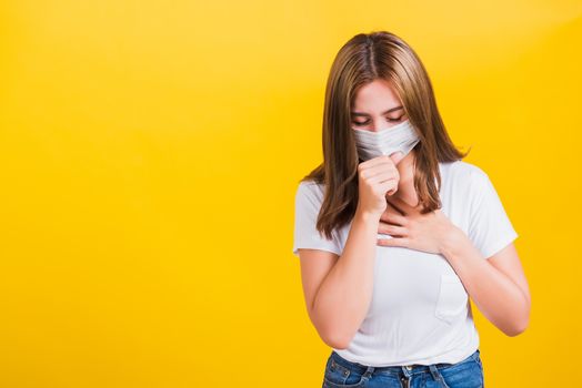 Asian portrait beautiful cute young woman standing wear t-shirt cough in mask protection from COVID virus epidemic or air pollution isolated, studio shot on yellow background with copy space