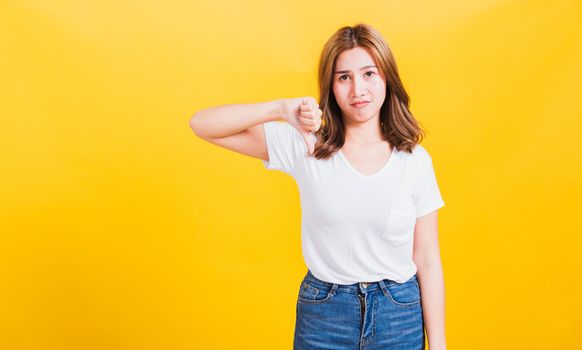 Portrait Asian Thai beautiful young woman unhappy, a negative gesture showing finger thumbs down or dislike sign, studio shot isolated on yellow background, There was copy space, rejection concept