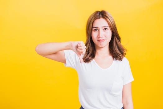 Portrait Asian Thai beautiful young woman unhappy, a negative gesture showing finger thumbs down or dislike sign, studio shot isolated on yellow background, There was copy space, rejection concept