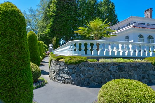 A perfect neighbourhood. Luxury residential house fenced with white balustrade built on land terrace decorated with topiary trees and bushes