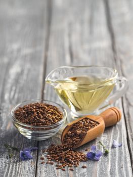 Flax seeds and flax oil. Brown linen seeds, flaxseed oil and blue flax flowers on old gray wooden background. Copy space. Vertical.