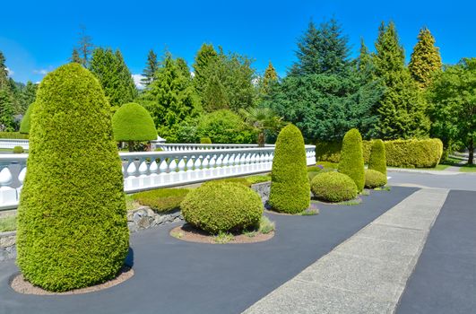 A perfect neighbourhood. Luxury residential house fenced with white balustrade built on land terrace decorated with topiary trees and bushes