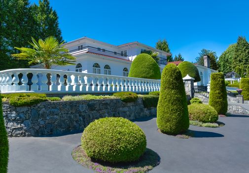 A perfect neighbourhood. Luxury residential house fenced with white balustrade built on land terrace decorated with topiary trees and bushes