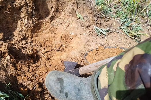 A man in rubber boots digs a shovel pit in a swamp. Finding water.