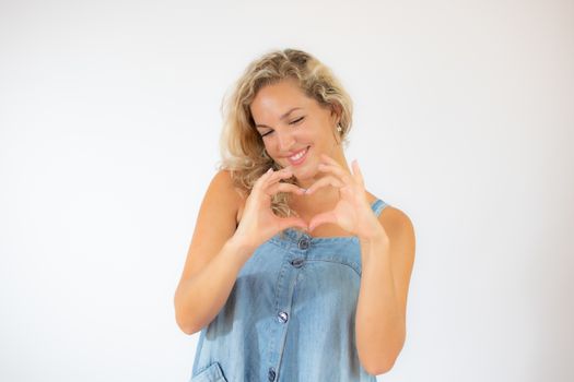 Pretty blonde woman in blue dress smiling making the heart figure