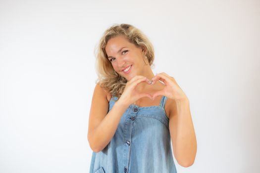 Pretty blonde woman in blue dress smiling making the heart figure