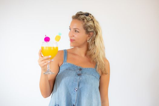 Pretty blonde woman in blue dress smiling with a fruit cocktail on white background