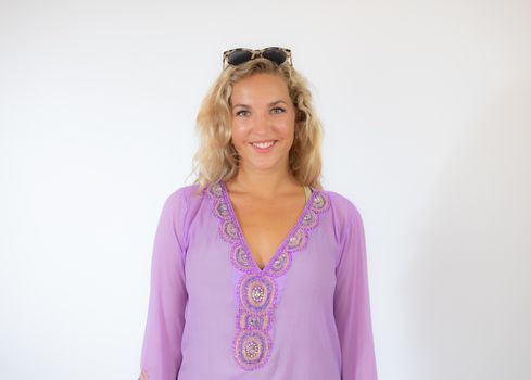 Pretty blonde woman wearing sunglasses and with a lilac caftan smiling