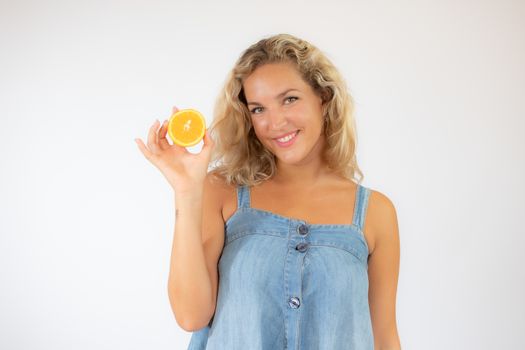 Pretty blonde woman in blue dress smiling with an orange in her hand