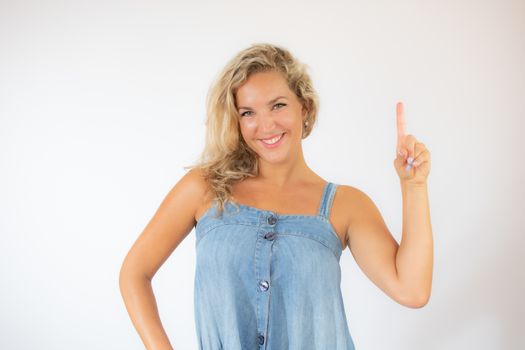 Pretty blonde woman in blue dress smiling pointing with her finger up