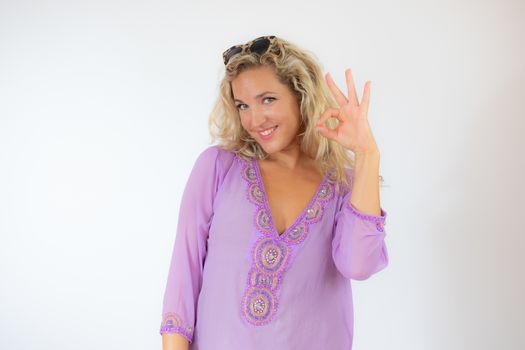 Pretty blonde woman in lilac caftan smiling and doing okay gesture