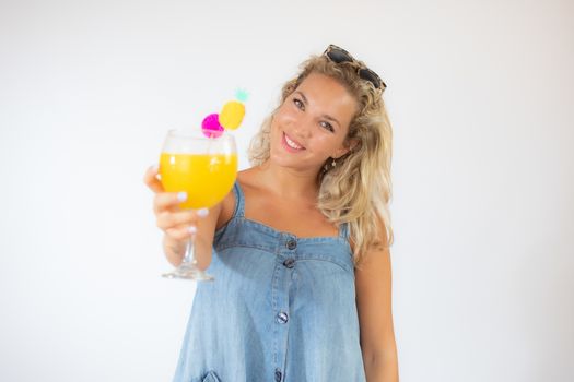 Pretty blonde woman in blue dress smiling with a fruit cocktail on white background