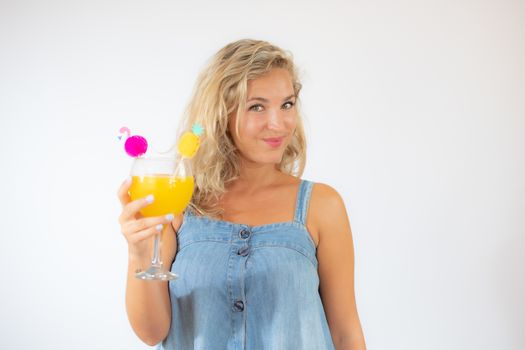 Pretty blonde woman in blue dress smiling with a fruit cocktail on white background