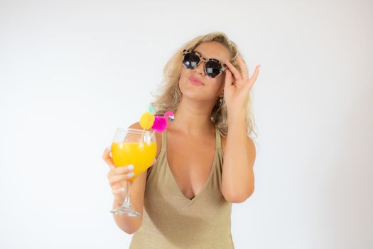 Pretty smiling blonde woman with sunglasses in golden swimsuit with a fruit cocktail