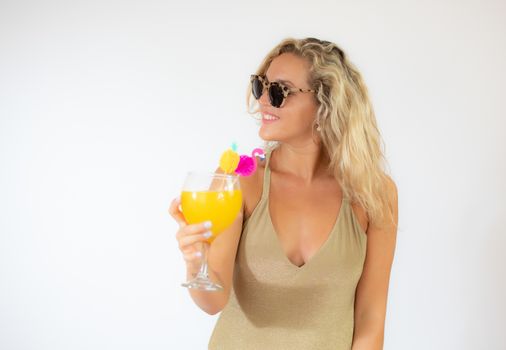 Pretty smiling blonde woman with sunglasses in golden swimsuit with a fruit cocktail