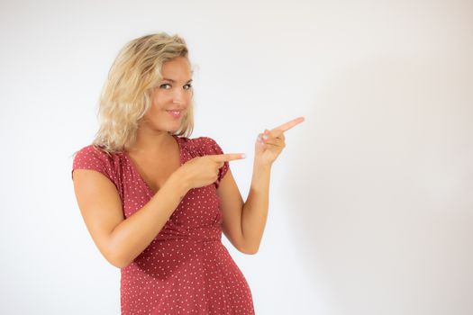 Beautiful smiling blonde woman in a red dress pointing something