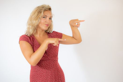 Beautiful smiling blonde woman in a red dress pointing something