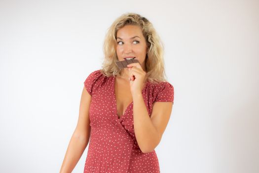 Beautiful smiling blonde woman in a red dress eating a piece of chocolate