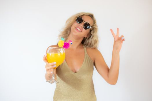 Pretty smiling blonde woman with sunglasses in golden swimsuit with a fruit cocktail