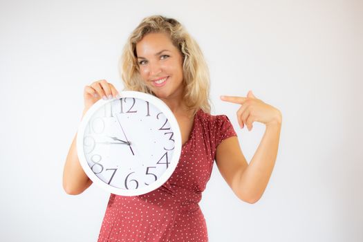 Pretty smiling blonde woman in red dress showing a big clock