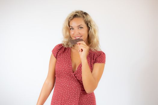 Beautiful smiling blonde woman in a red dress eating a piece of chocolate