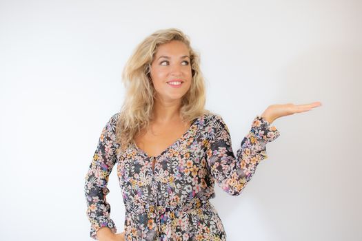 Pretty blonde woman in a flowery dress gesturing on white background