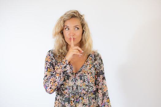 Pretty blonde woman in a flowery dress gesturing on white background