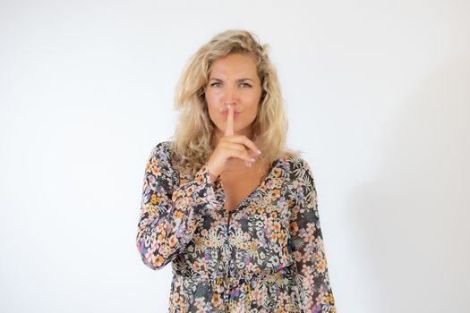 Pretty blonde woman in a flowery dress gesturing on white background