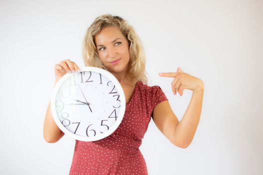 Pretty smiling blonde woman in red dress showing a big clock