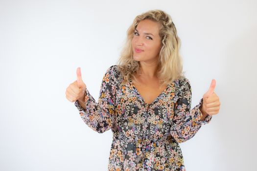 Pretty blonde woman in a flowery dress gesturing on white background