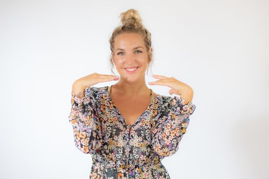 Pretty blonde woman in a flowery dress gesturing on white background