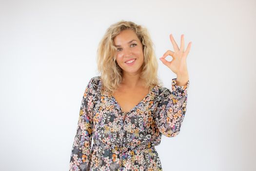 Pretty blonde woman in a flowery dress gesturing on white background