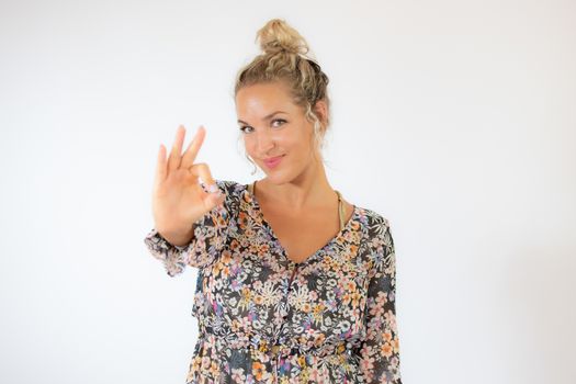 Pretty blonde woman in a flowery dress gesturing on white background