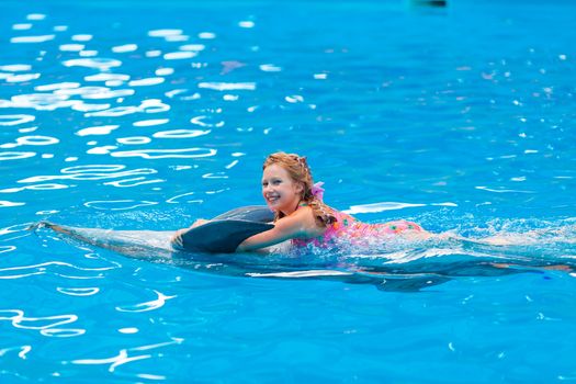 Happy little girl swimming with dolphins in Dolphinarium. Swimming, bathing and communication with dolphins.