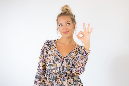 Pretty blonde woman in a flowery dress gesturing on white background