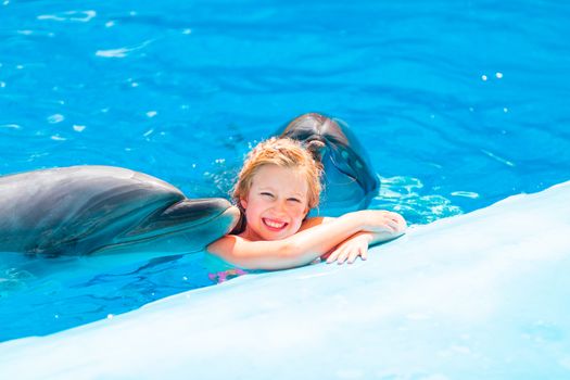 Happy little girl swimming with dolphins in Dolphinarium. Swimming, bathing and communication with dolphins.