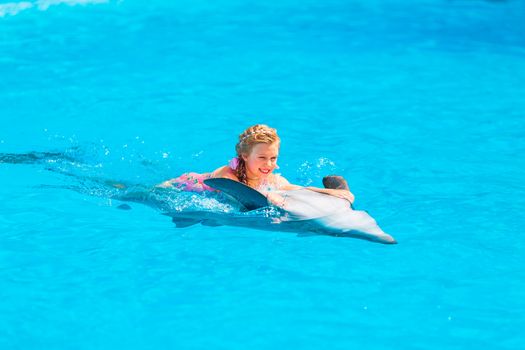 Happy little girl swimming with dolphins in Dolphinarium. Swimming, bathing and communication with dolphins.