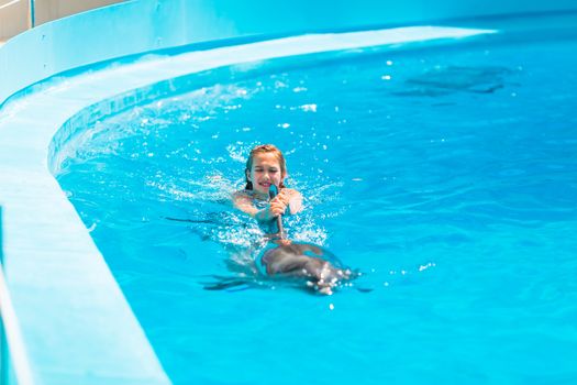 Happy little girl swimming with dolphins in Dolphinarium. Swimming, bathing and communication with dolphins.