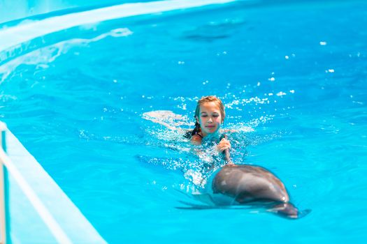 Happy little girl swimming with dolphins in Dolphinarium. Swimming, bathing and communication with dolphins.